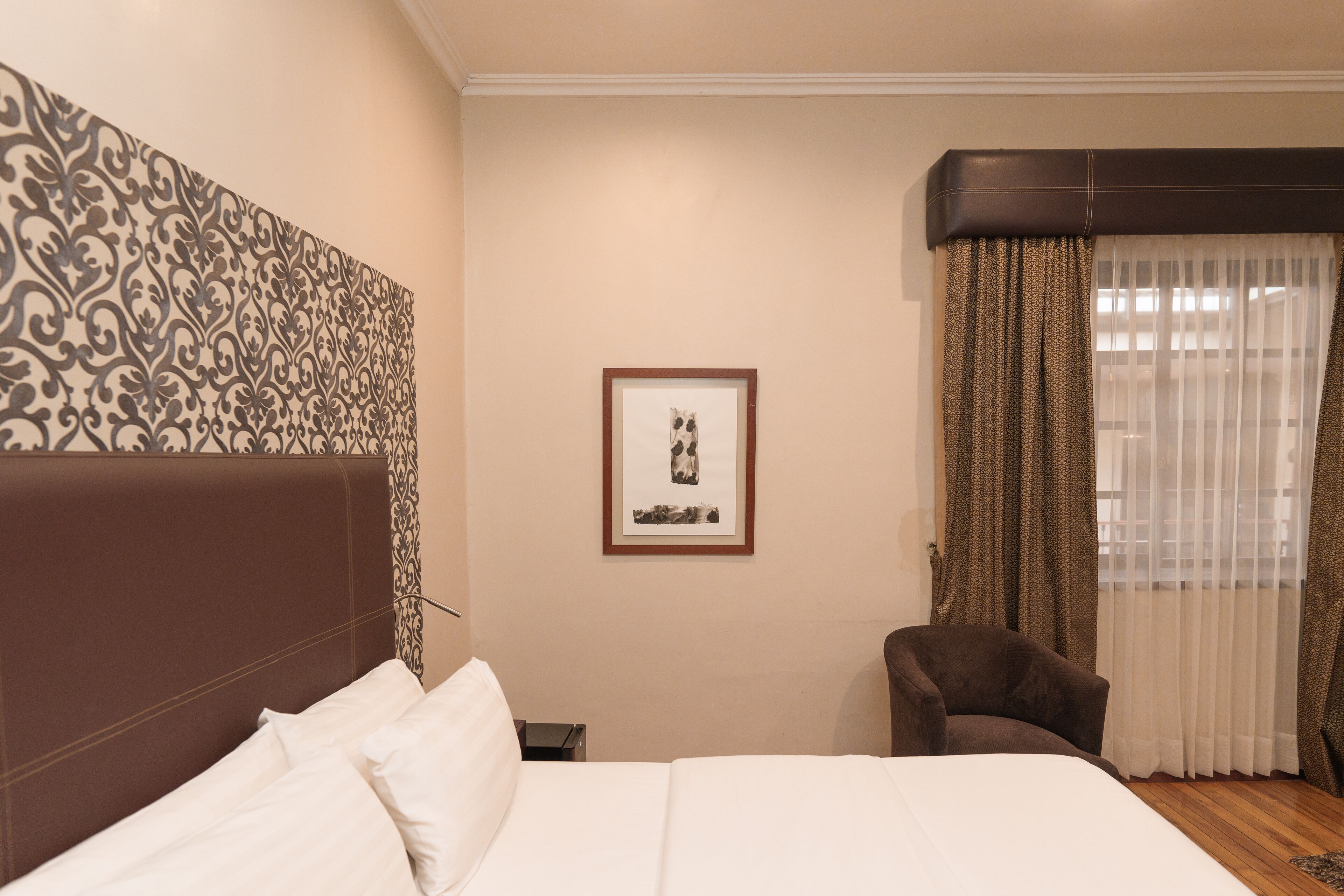 A hotel room with a large bed, a chair, a framed picture on the wall, and a window with curtains.