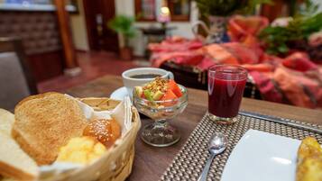 A breakfast setting with bread, a fruit bowl, a cup of coffee, and a glass of juice on a table.
