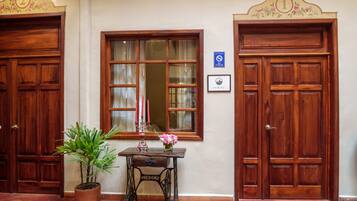 A hallway with two wooden doors, a window with a mirror, a table with a potted plant and a vase of flowers, and a sign indicating a no-smoking area.