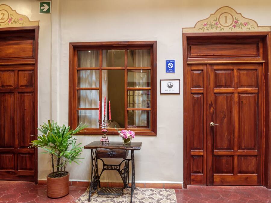 A hallway with two wooden doors, a window with a mirror, a table with a potted plant and a vase of flowers, and a sign indicating a no-smoking area.