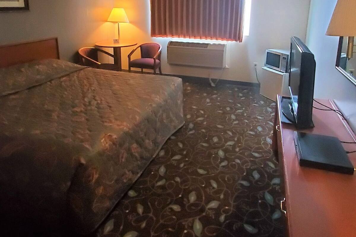 Une chambre d’hôtel comprenant un lit, un bureau avec un ordinateur, une chaise, une lampe, un téléviseur et une fenêtre avec des rideaux.