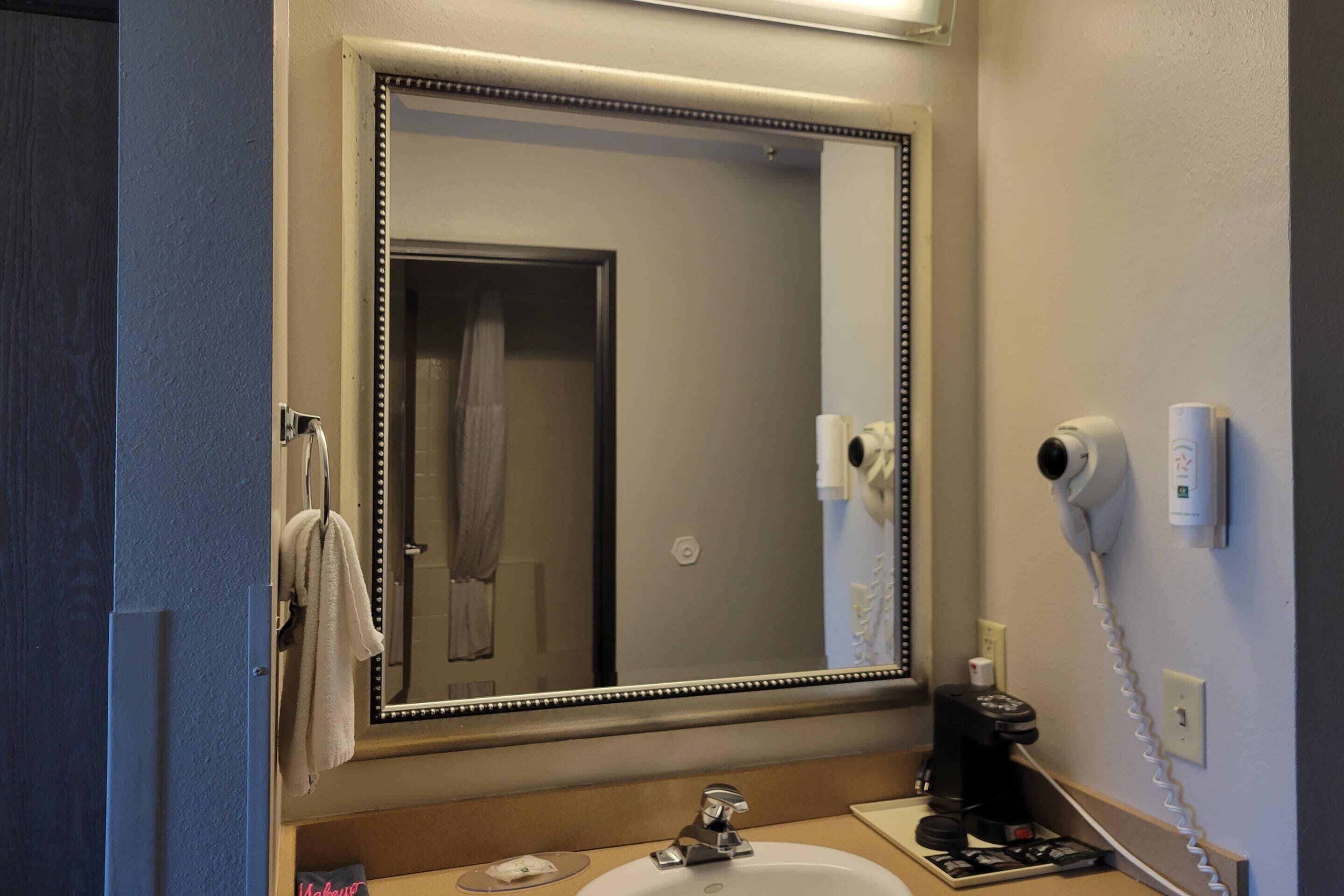 A bathroom with a large mirror, a sink, a towel rack, a hairdryer, and a telephone.