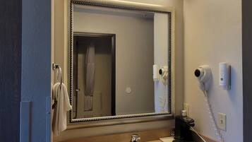 A bathroom with a large mirror, a sink, a towel rack, a hairdryer, and a telephone.