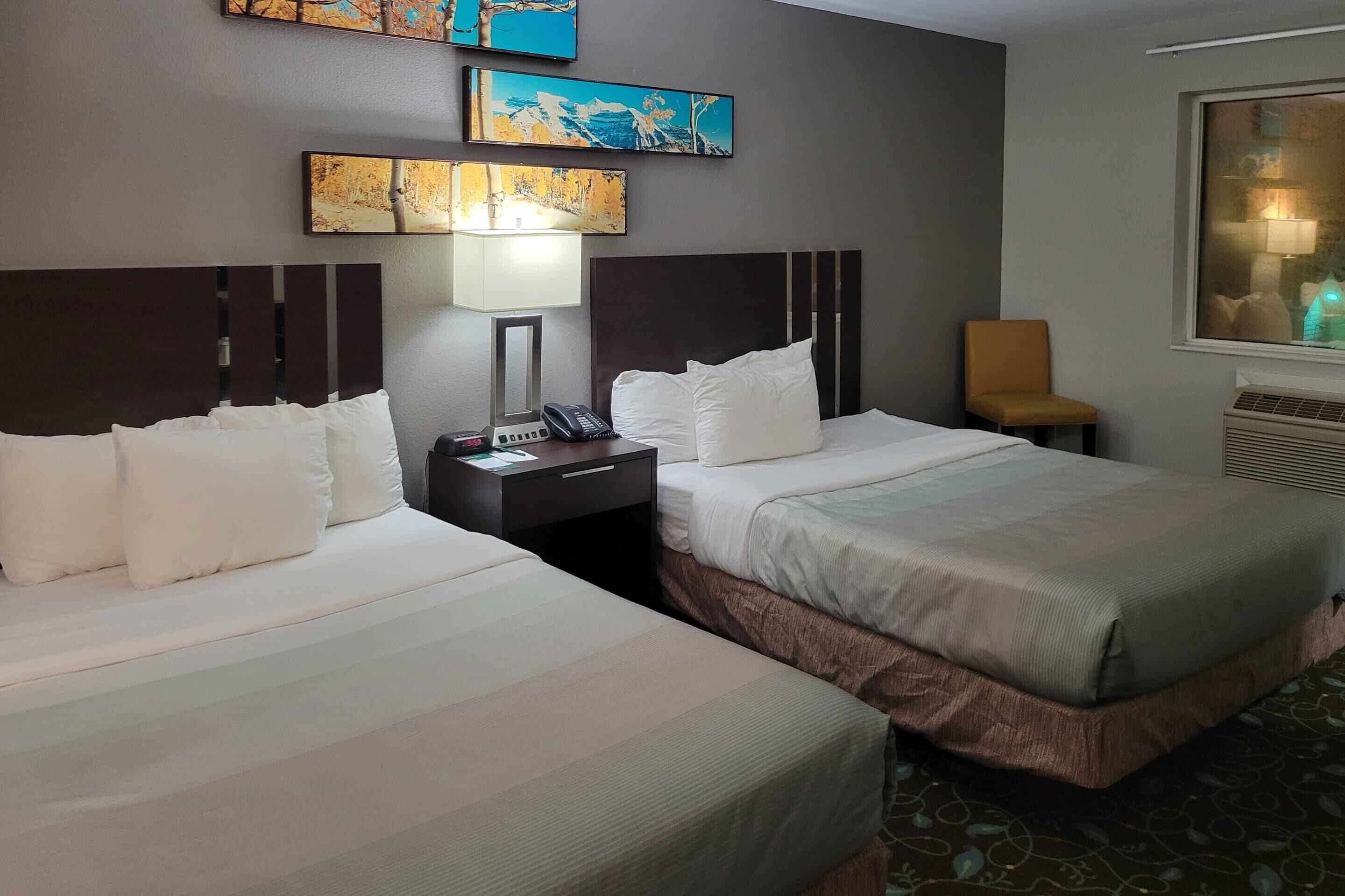 A hotel room with two beds, a nightstand with a phone, a chair, and artwork on the wall.