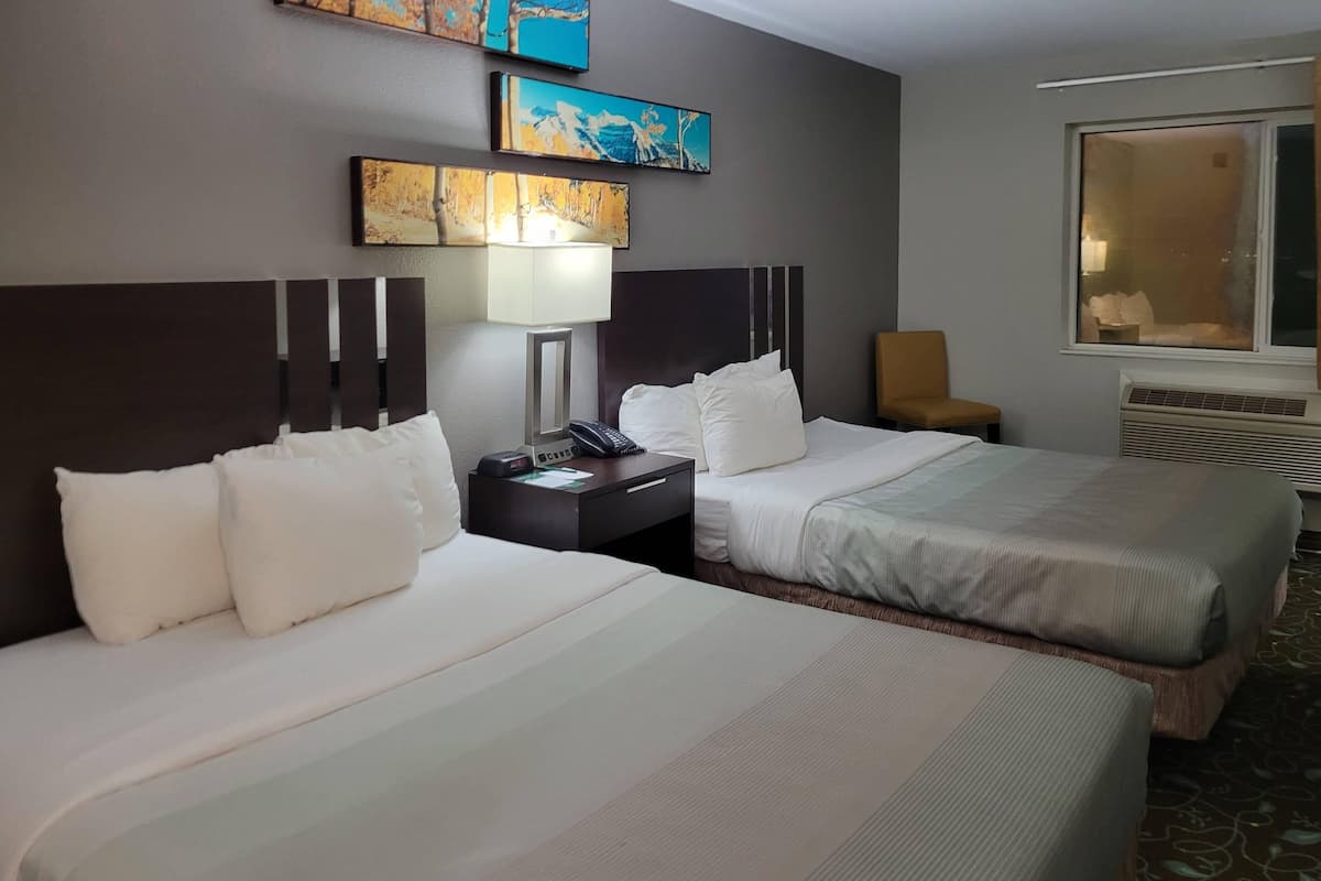 Une chambre d’hôtel avec deux lits, une table de chevet avec une lampe, une chaise et des œuvres d’art accrochées au mur.