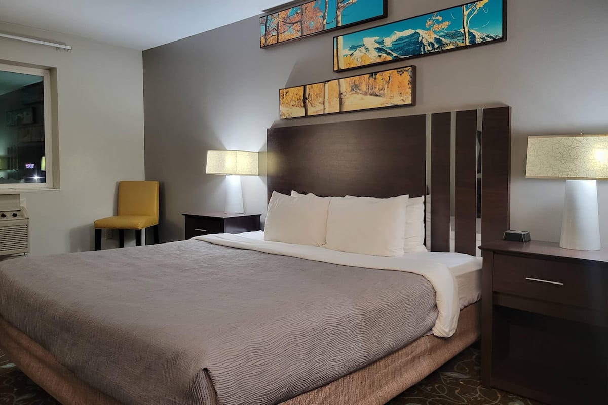 Une chambre d’hôtel avec un grand lit, une table de chevet, une chaise, une lampe et des œuvres d’art accrochées au mur.