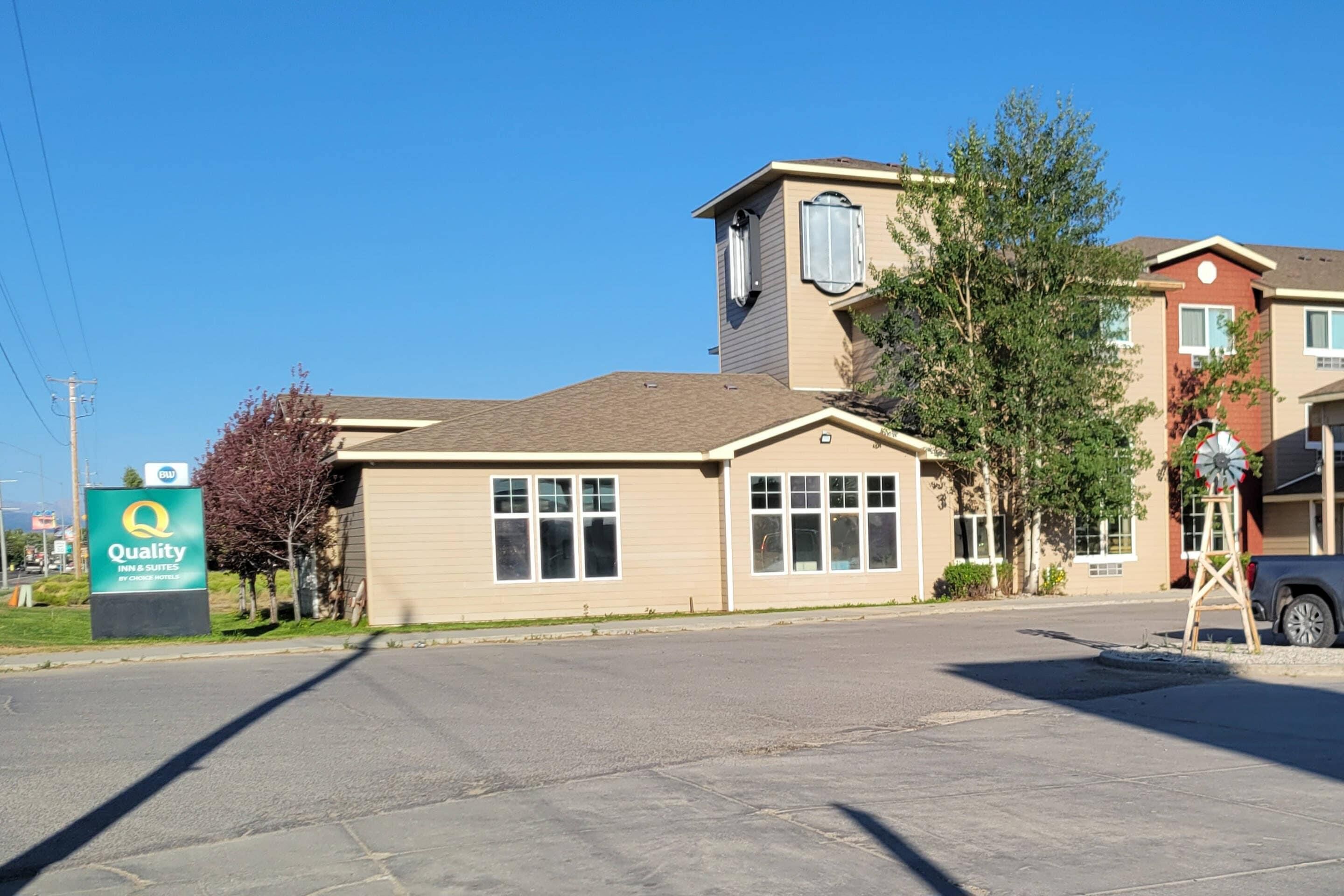 A hotel with a sign for 'Quality Inn & Suites by Choice Hotels,' a two-story building with a flat roof, and a parked car in the foreground.