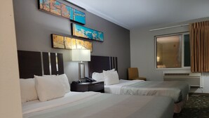A hotel room with two beds, a bedside table with a lamp, a chair, and artwork on the wall. - Quality Inn & Suites Pinedale (Pinedale)