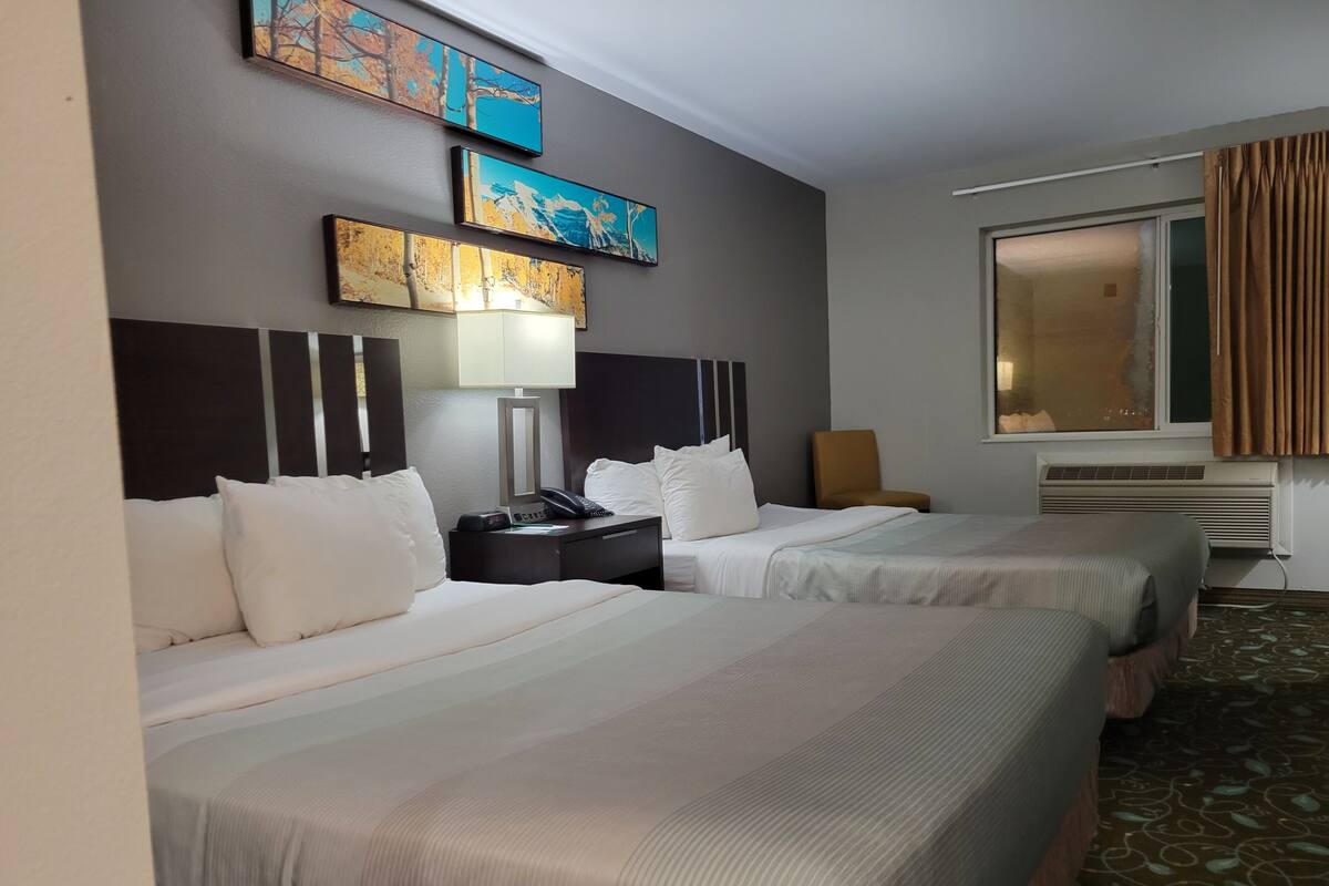 Une chambre d’hôtel avec deux lits, une table de chevet avec une lampe, une chaise et des œuvres d’art accrochées au mur.