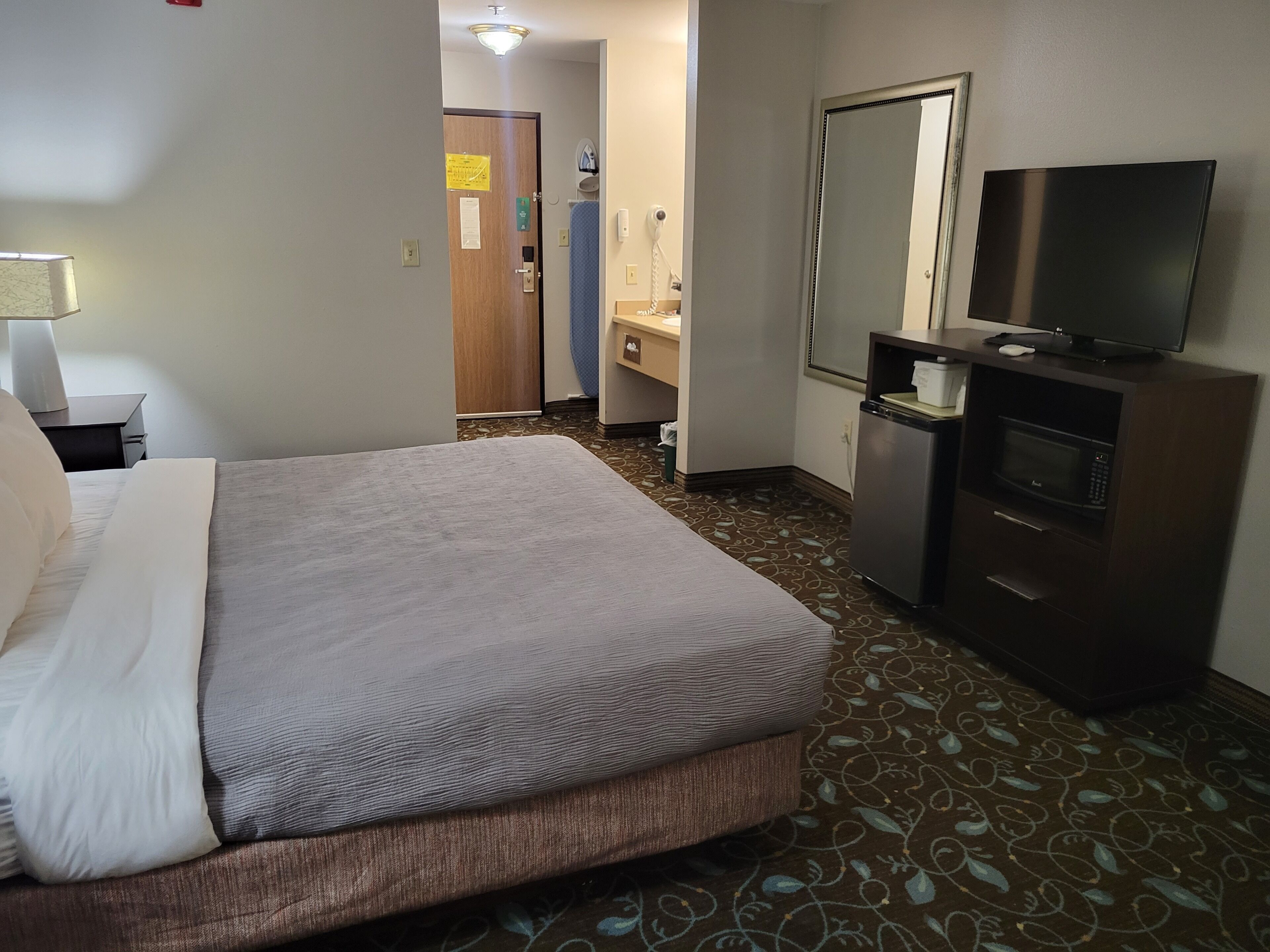 Een hotelkamer met een bed, een televisie, een bureau, een spiegel en een badkamer.