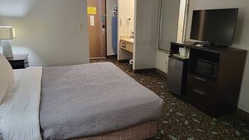 Een hotelkamer met een bed, een televisie, een bureau, een spiegel en een badkamer.