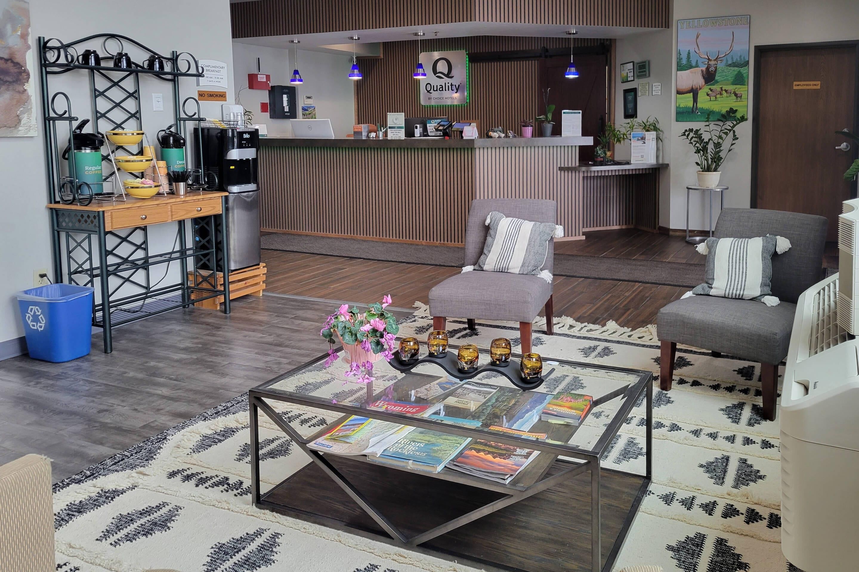 Zona de recepción con mostrador, estación de café, área de descanso con dos sillones y una mesa baja de vidrio con revistas.
