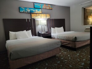 A hotel room with two beds, a nightstand, a lamp, and artwork on the wall. - Quality Inn & Suites Pinedale (Pinedale)