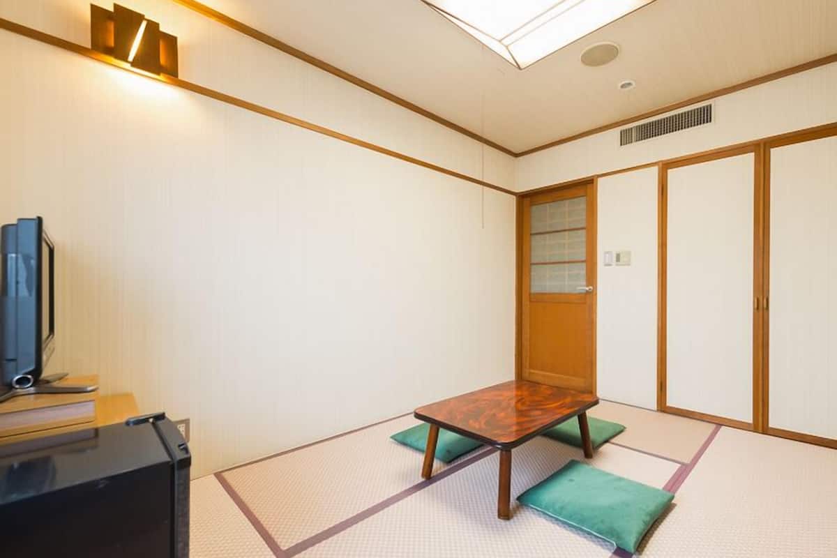 A traditional Japanese room with tatami flooring, a low wooden table, and a television on a stand.