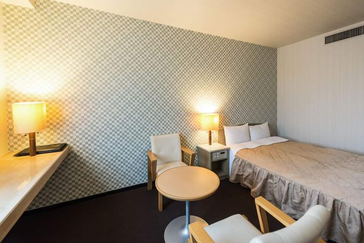 A hotel room with a bed, two chairs, a small table, and two bedside lamps.