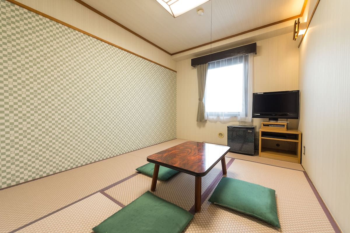 A traditional Japanese room with tatami flooring, a low wooden table with cushions, a television, and a sliding door.