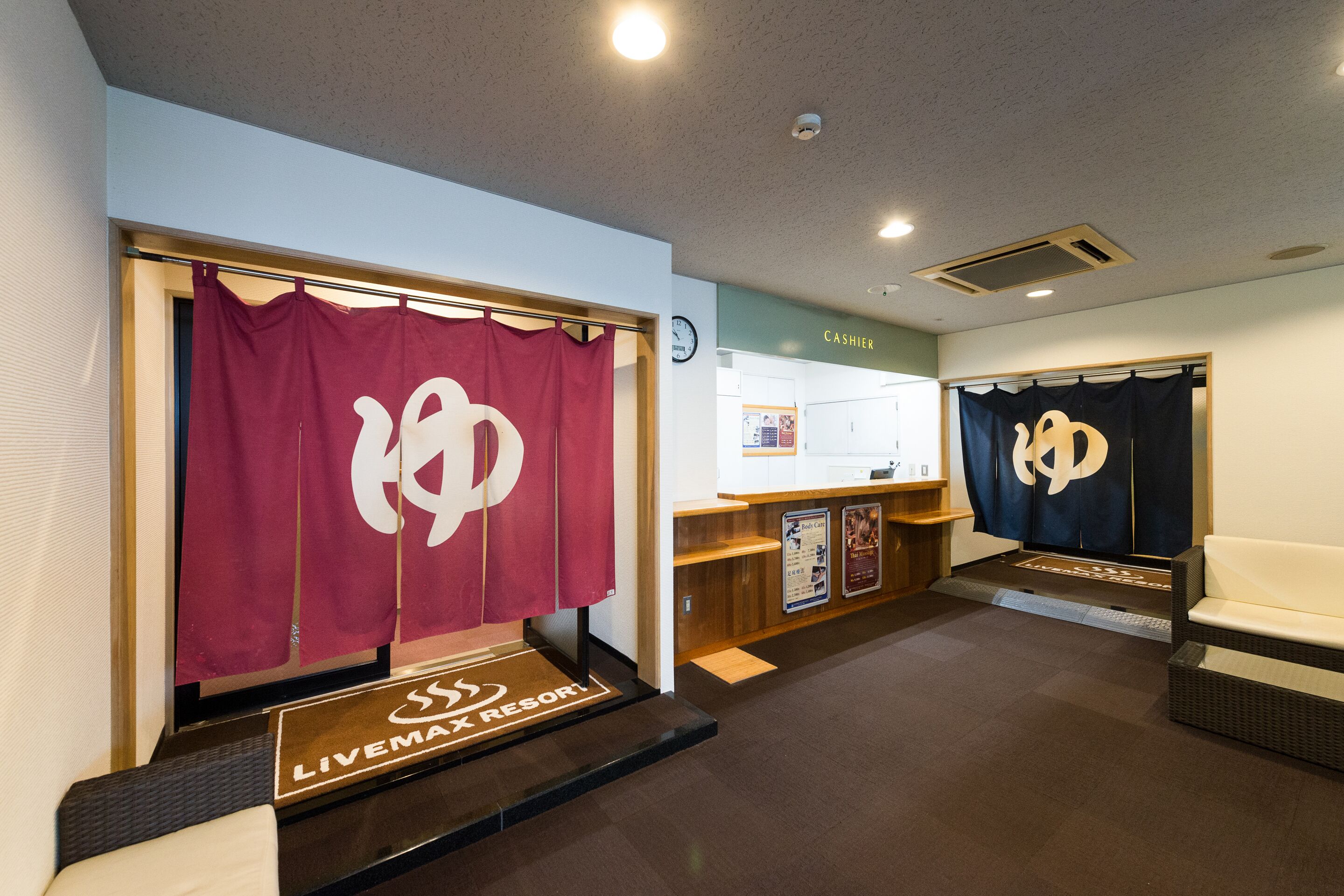 A hotel lobby with a reception desk, a clock, and two seating areas with curtains.