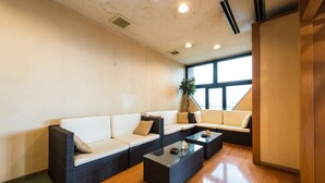 A modern lounge area with a sectional sofa, a coffee table, and a potted plant. - Hotel LiVEMAX Kofu (Kai)