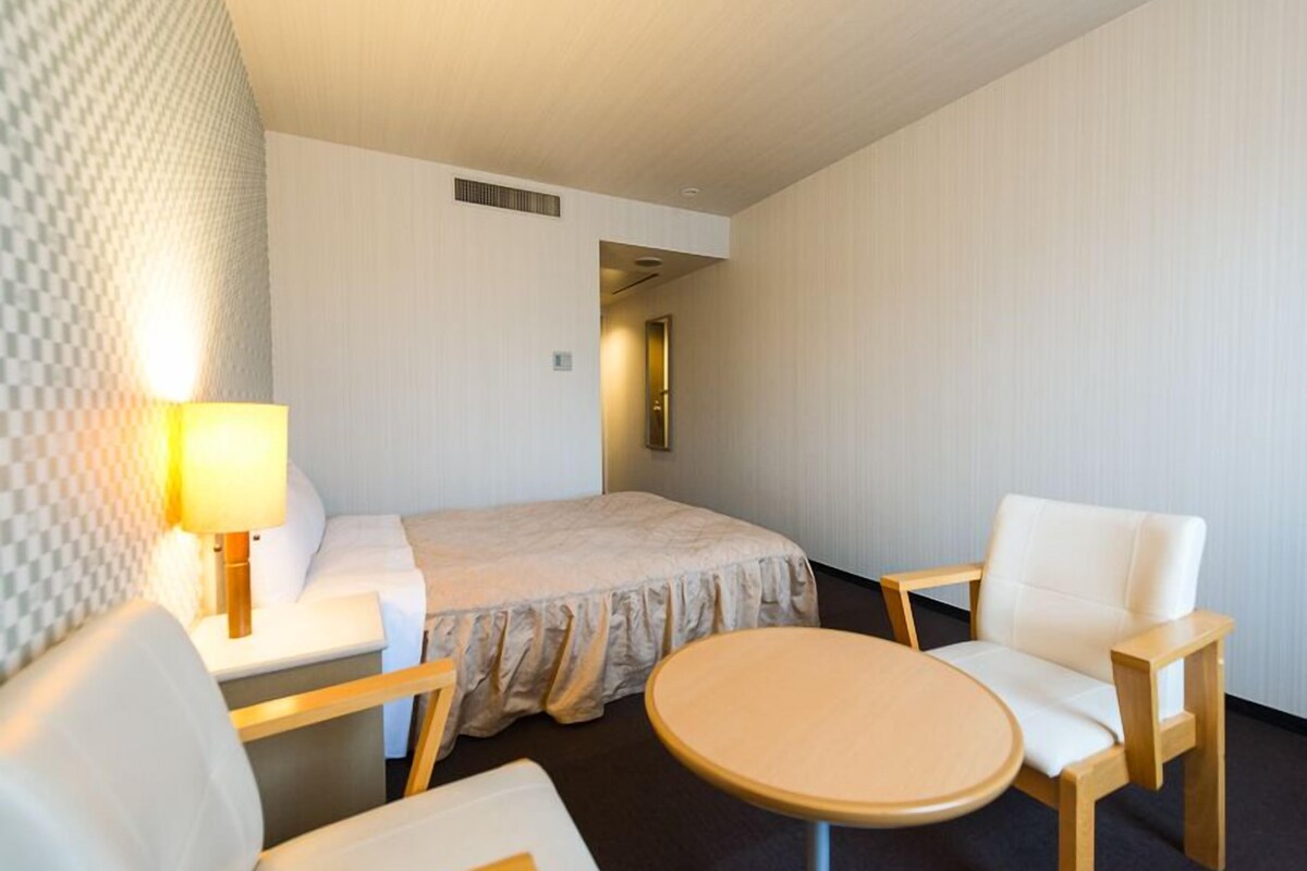 A hotel room with a bed, two chairs, a small table, a lamp, and a mirror.