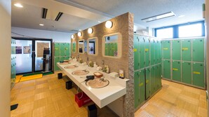 A public restroom with multiple sinks, green lockers, and a mirror wall. - Hotel LiVEMAX Kofu (Kai)