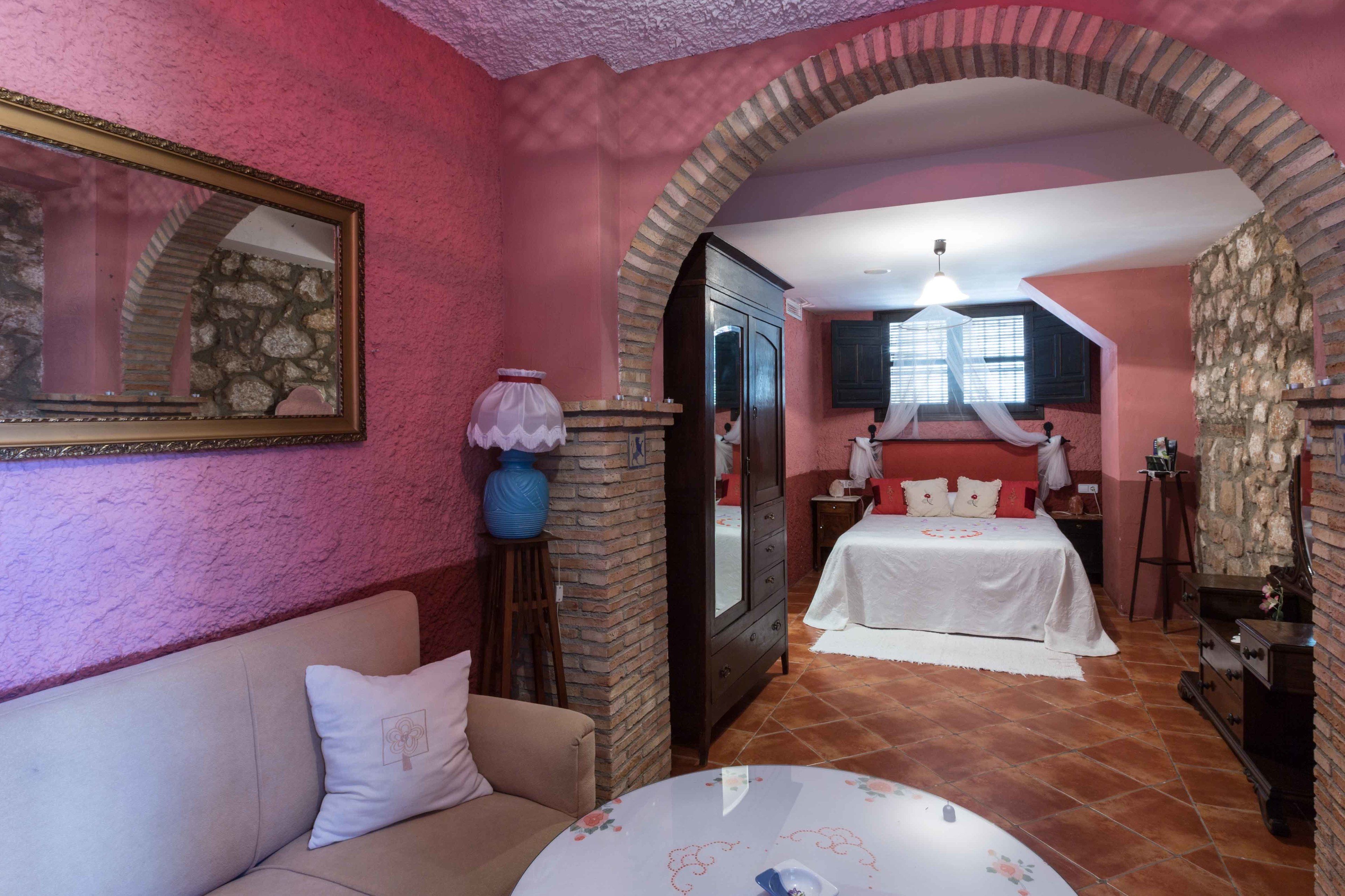 A room with a stone fireplace, a bed with white bedding, a sofa with a cushion, and a table with a floral tablecloth.