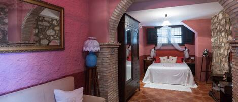 A room with a stone fireplace, a bed with white bedding, a sofa with a cushion, and a table with a floral tablecloth.