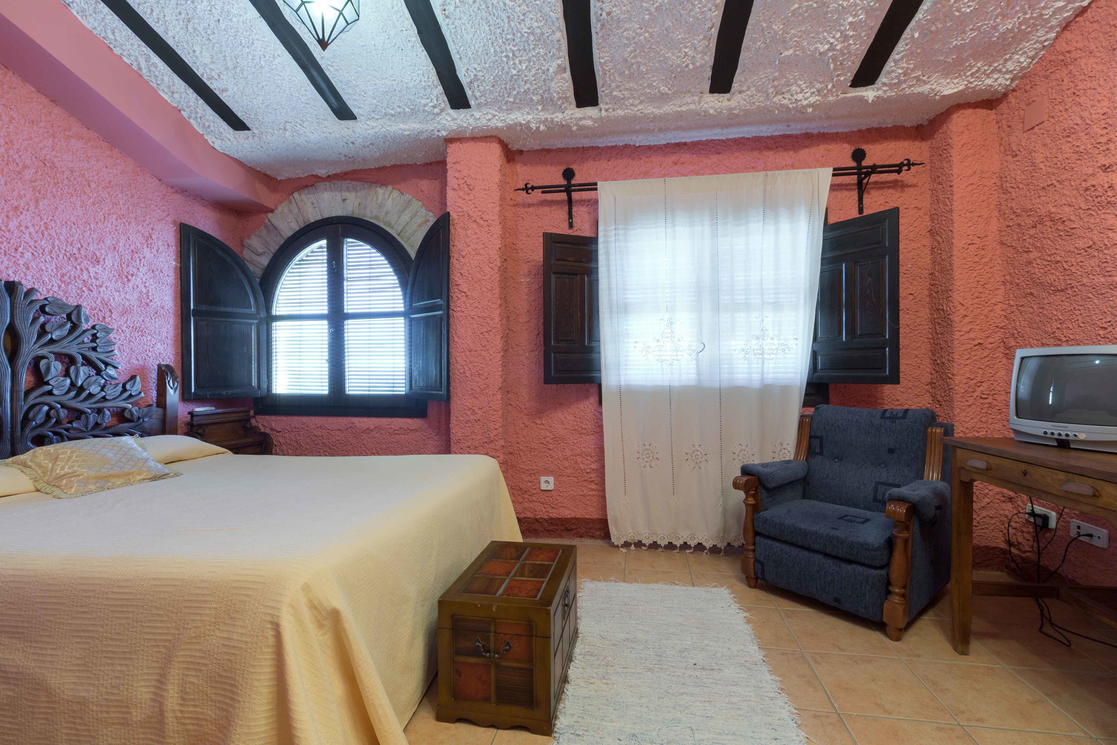 A bedroom with a bed, a chair, a television, and a small wooden chest.
