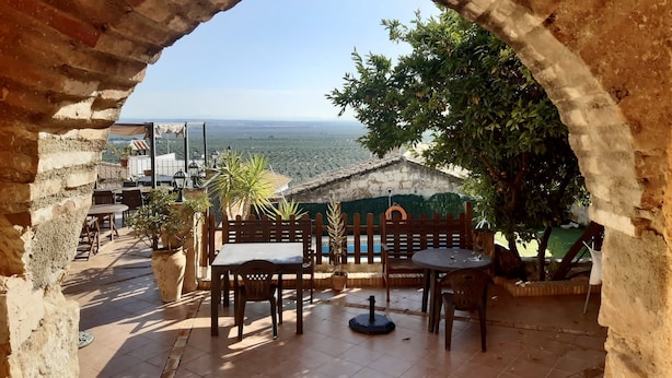 Eine Terrasse im Freien mit Blick auf eine weite Landschaft, inklusive eines Steinbogen, Holztische und Stühle.