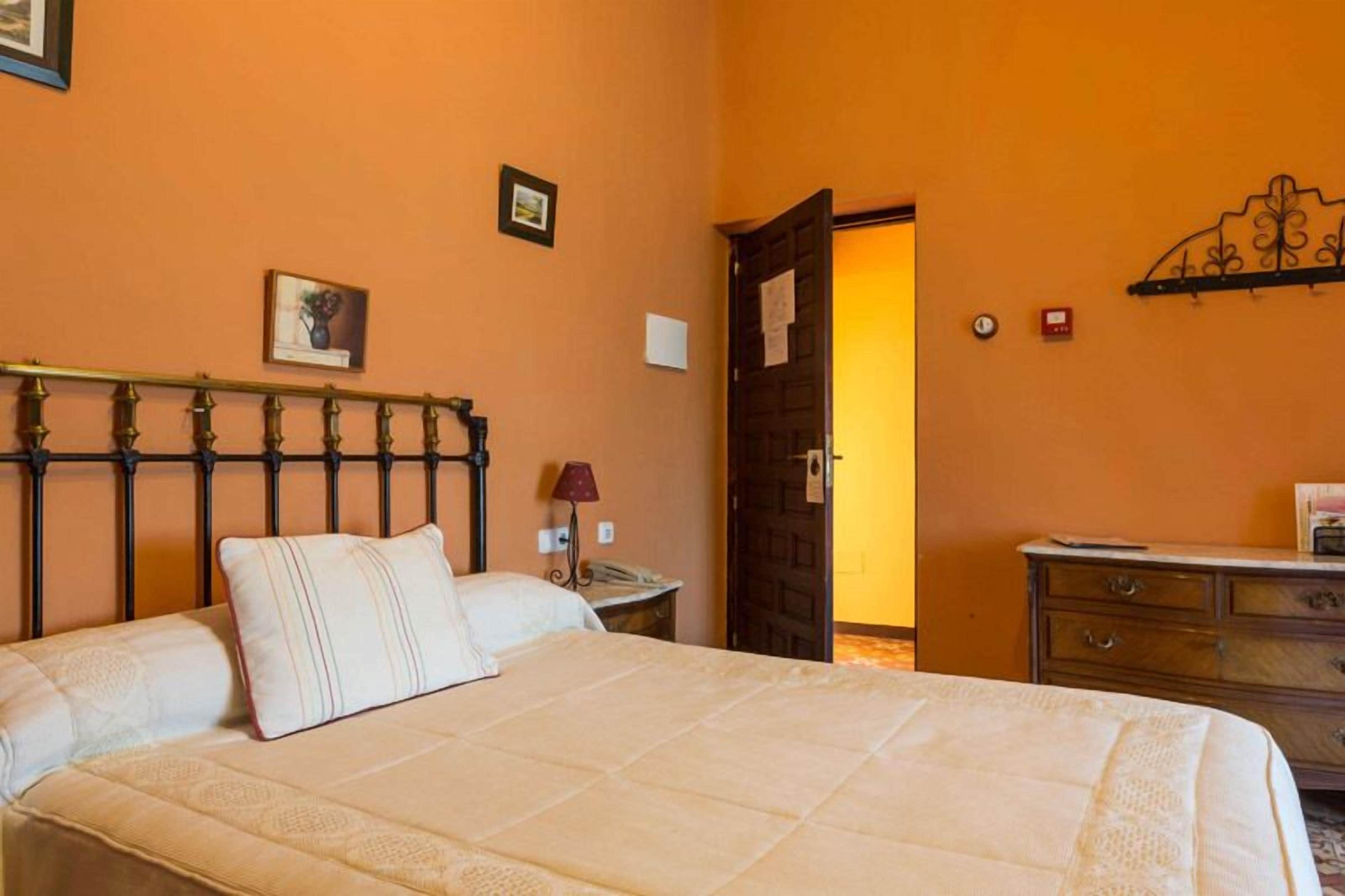 Un dormitorio con cama, mesita de noche, cómoda y una puerta que da a otra habitación.