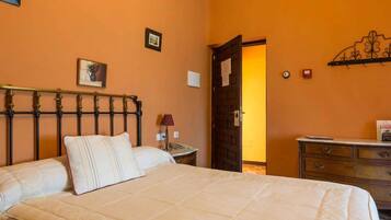 Un dormitorio con cama, mesita de noche, cómoda y una puerta que da a otra habitación.