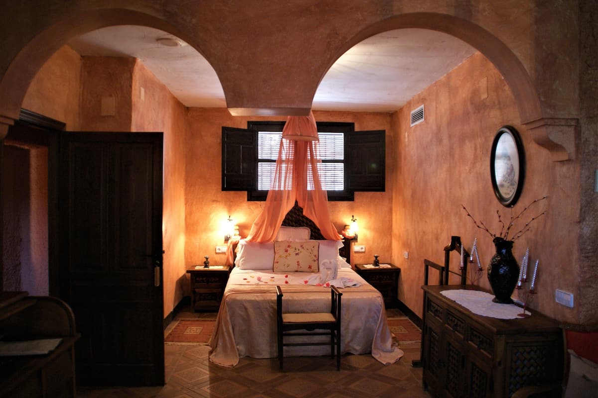 Um quarto com cama de dossel, mesa de cabeceira de madeira, mesa de apoio e cômoda.