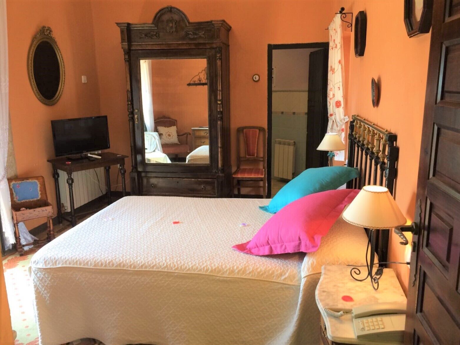 Ein Schlafzimmer mit einem Bett, einem Spiegel, einem Fernseher, einem Sessel und einer Lampe.