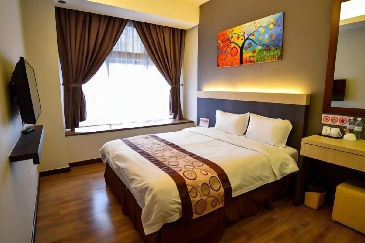 A hotel room with a bed, a desk, a mirror, and a painting on the wall.