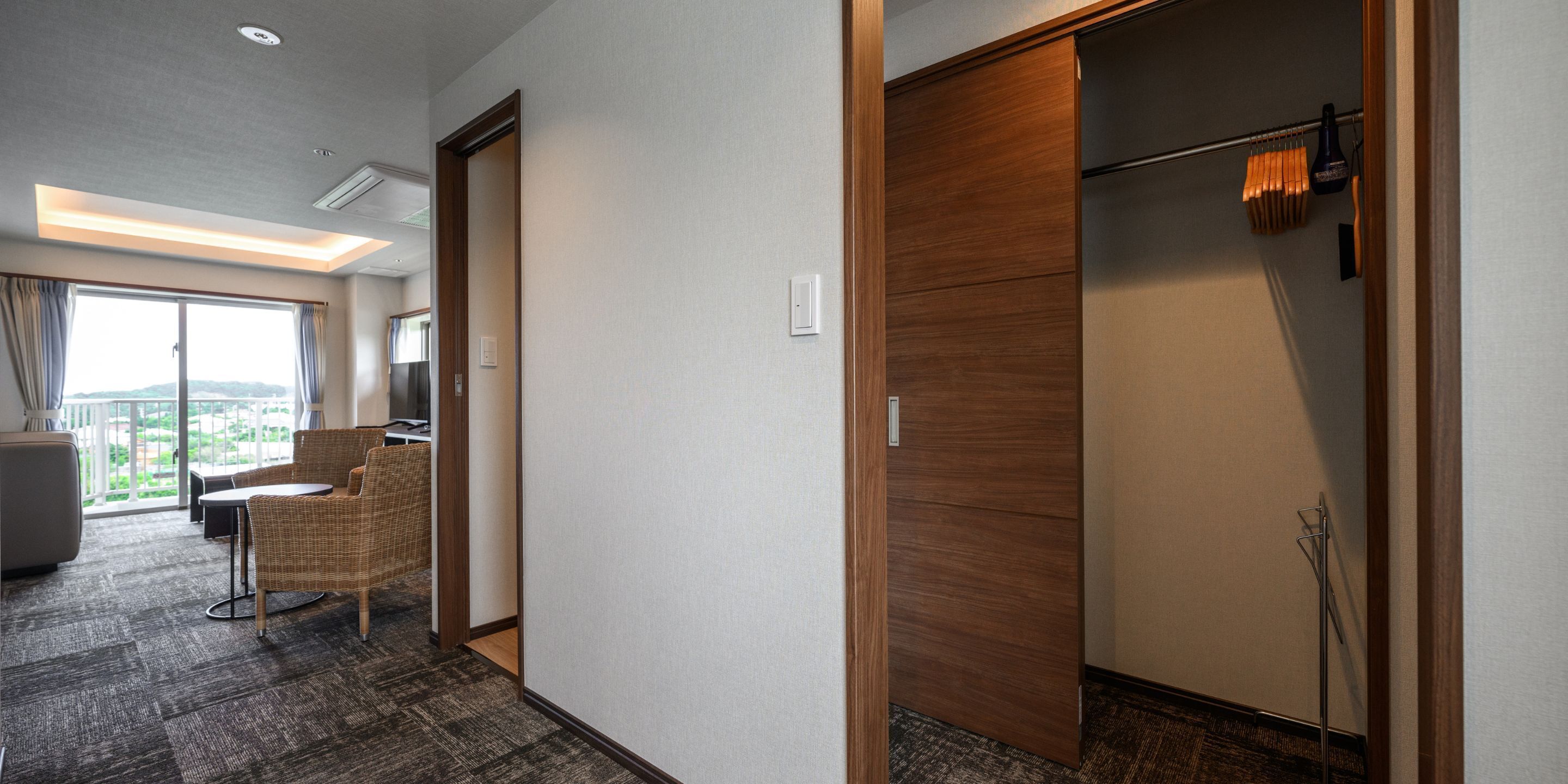 A hotel room with a balcony, a sofa, a dining table, and a wardrobe.