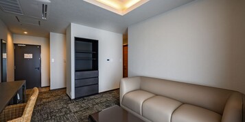 Habitación de hotel moderna con sofá, mesa de comedor, silla de mimbre, armario empotrado y piso alfombrado.