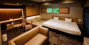 Habitación de hotel con cama, zona de estar con una silla, una mesita, un escritorio y ventana con vista a zonas verdes.