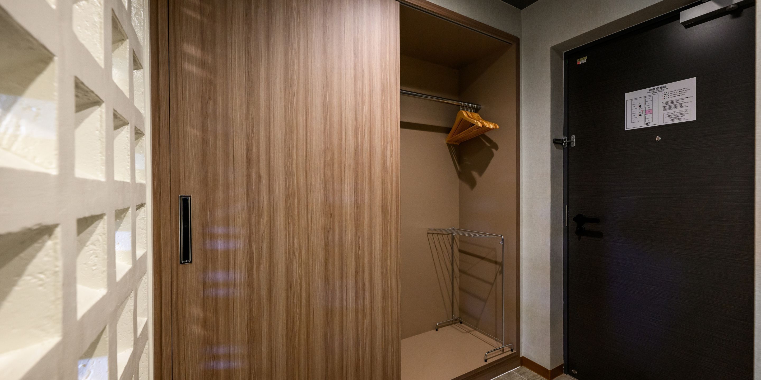 A hotel room with a wooden wardrobe, a metal drying rack, and a dark door.