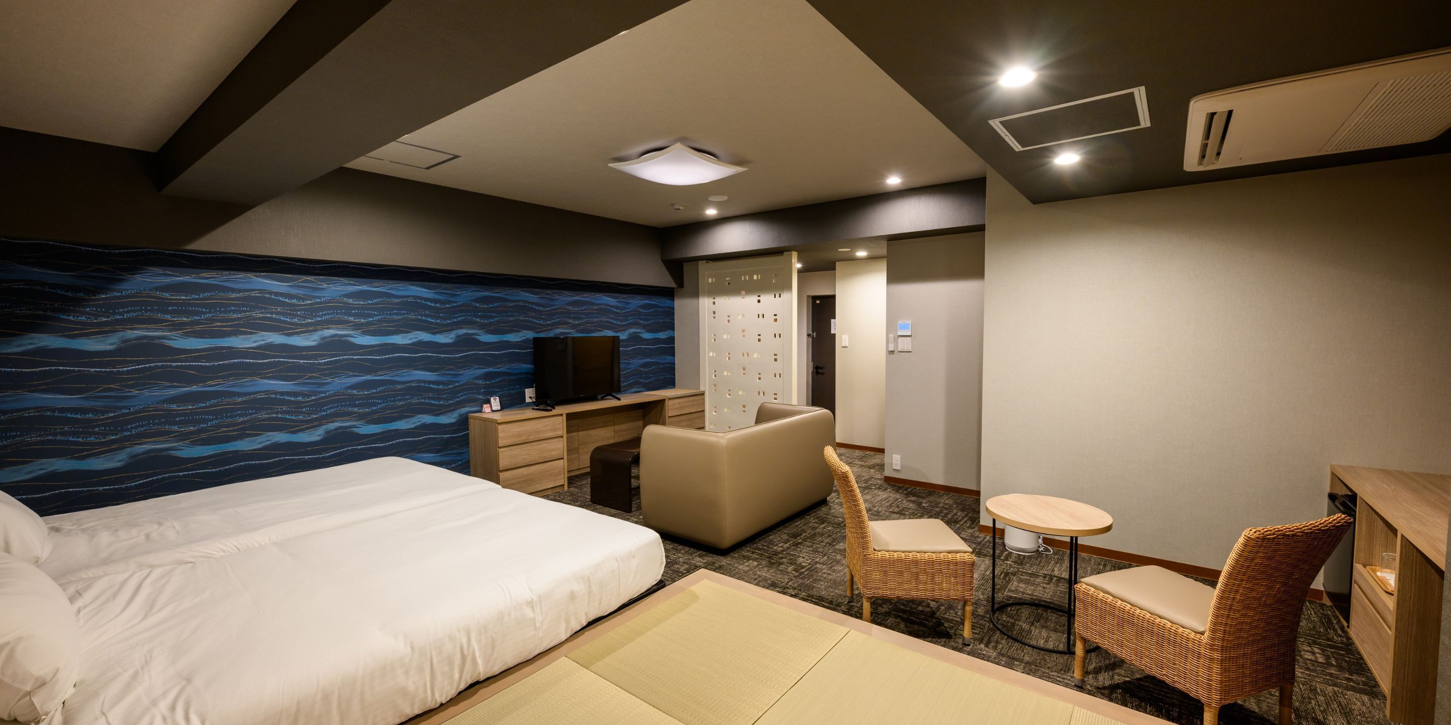 Ein Hotelzimmer mit Bett, Schreibtisch, Stuhl, einem kleinen Tisch und einer Wand mit blauem Wellenmuster.