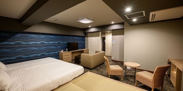 Habitación de hotel con cama, escritorio, silla, una mesita y pared con un diseño de olas azules.