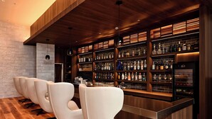 A bar area with a wooden ceiling, a brick wall, and a bar counter with bottles. There are four white chairs in front of the bar. - Lit Hotel NAKIJIN (Nakijin)