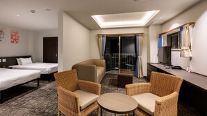 Ein Hotelzimmer mit zwei Einzelbetten, einem Schlafsofa, zwei Korbsesseln, einem kleinen Tisch, einem Schreibtisch mit Computer und einem Balkon mit Vorhängen.