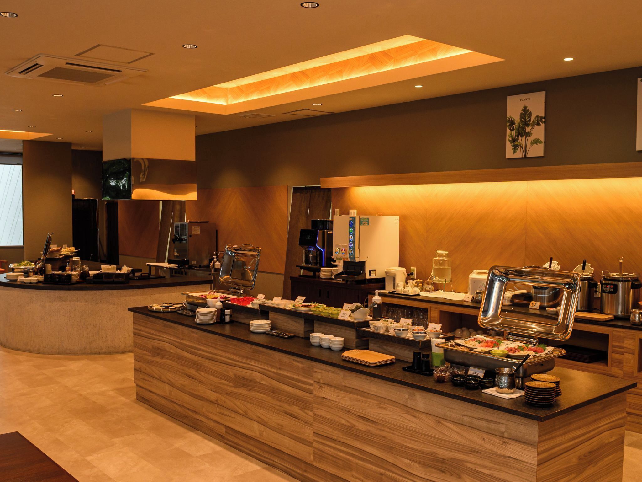 A modern hotel breakfast area with a central counter, buffet, and coffee station.