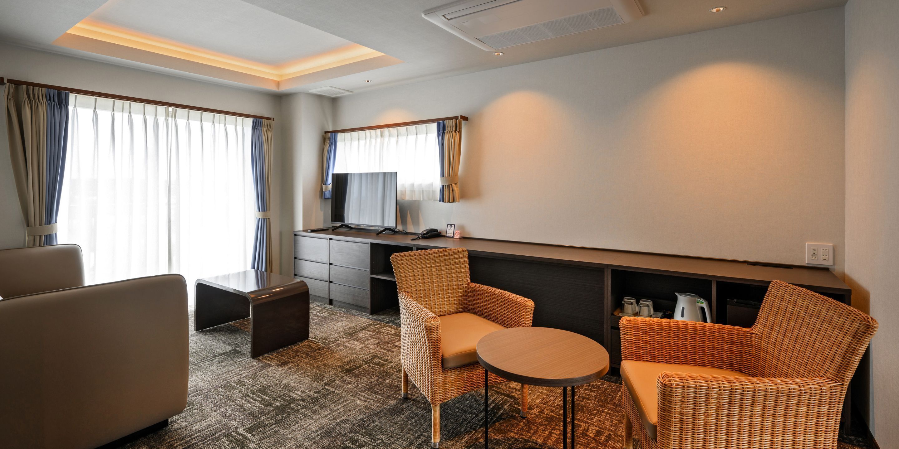 A hotel room with a sofa, armchair, small round table, and a desk with a mirror.