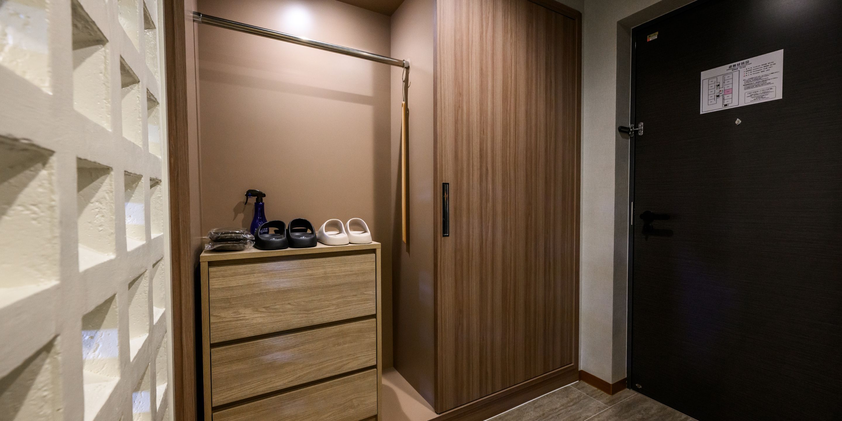 Un couloir avec une armoire en bois, un porte-chaussures contenant différentes paires de chaussures et une porte avec une pancarte.