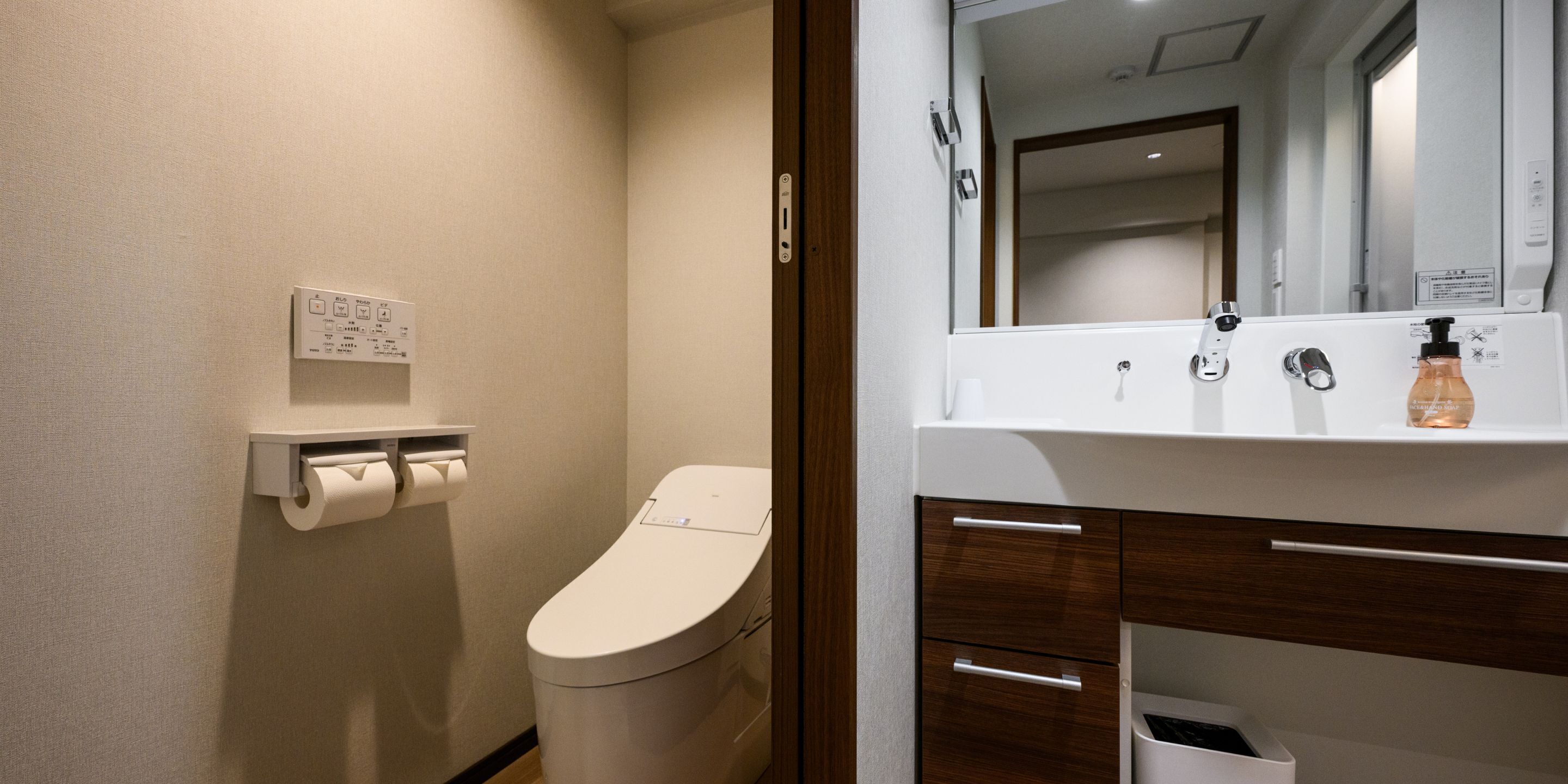 A modern bathroom with a toilet, a hand dryer, a soap dispenser, and a mirror above the sink.
