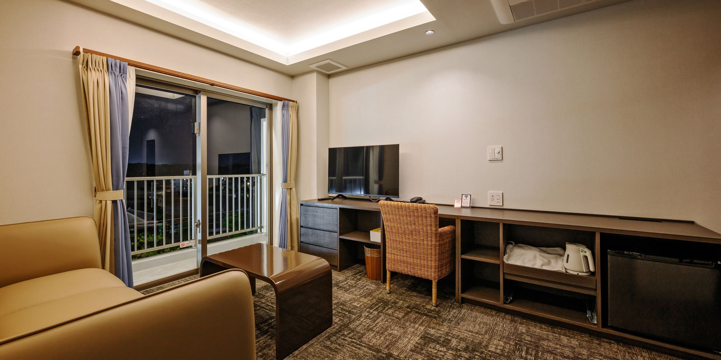 Habitación de hotel con balcón, escritorio, silla, televisor y minibar.