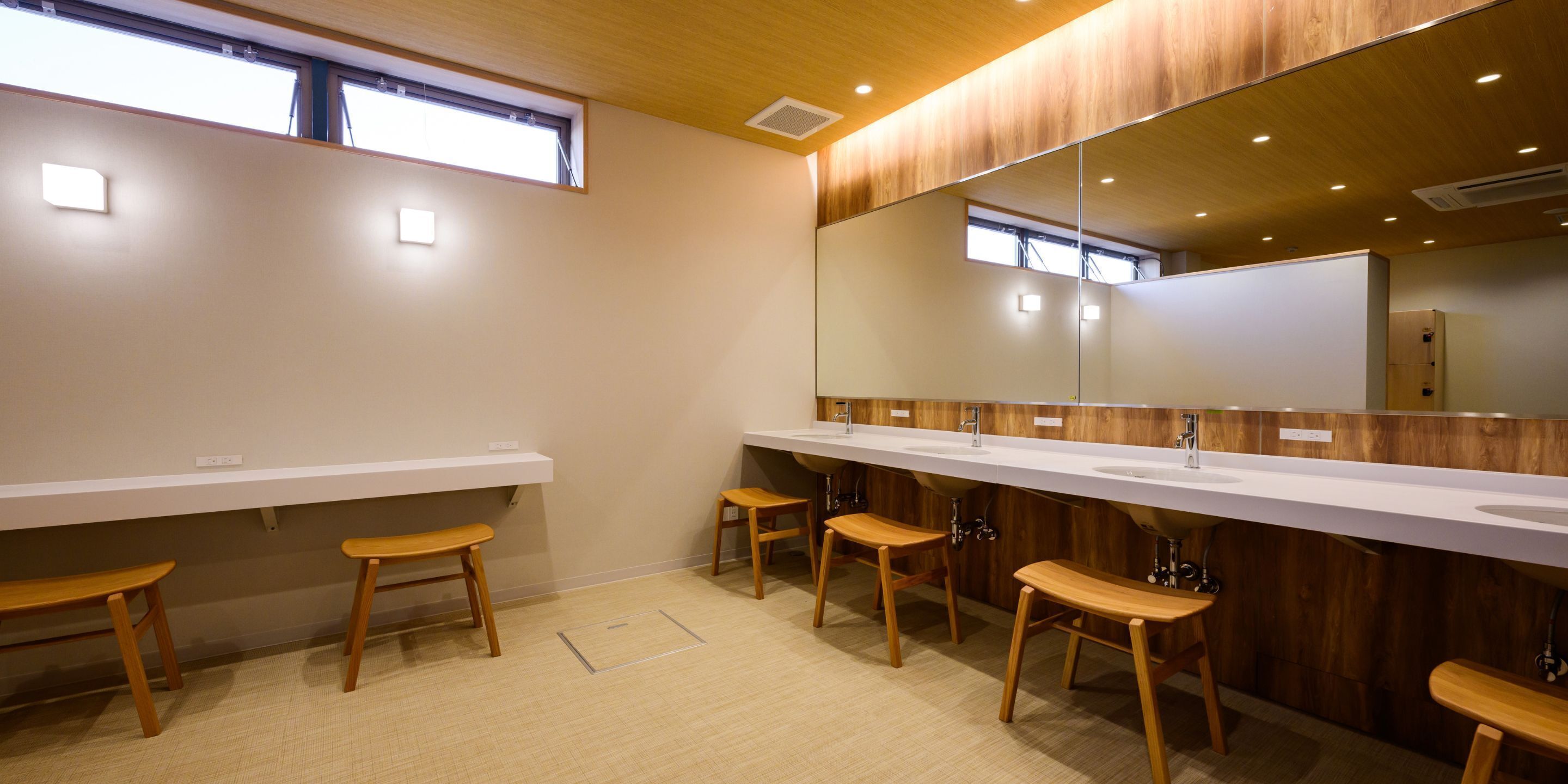 Une salle de bain moderne avec des bancs en bois, un long plan de vasque et un grand miroir.
