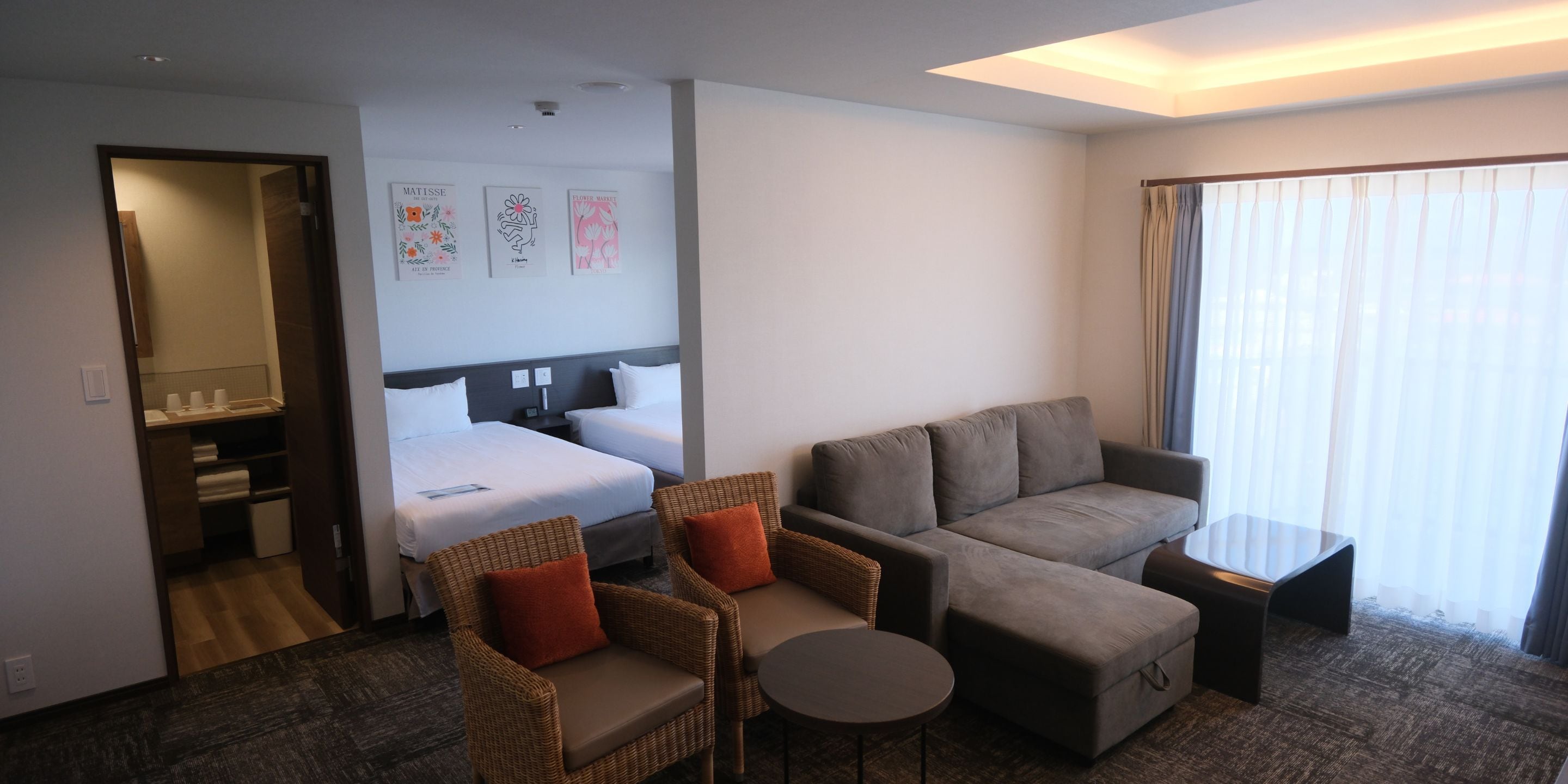 Une chambre d’hôtel avec un lit, deux canapés, une petite table et une salle de bain visible à travers une porte ouverte.