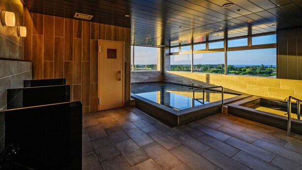 A modern spa area with a glass-enclosed hot tub, wooden panel walls, and large windows offering a view of the cityscape. - Lit Hotel NAKIJIN (Nakijin)