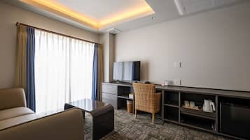 A hotel room with a sofa, a desk, a television, and a minibar.